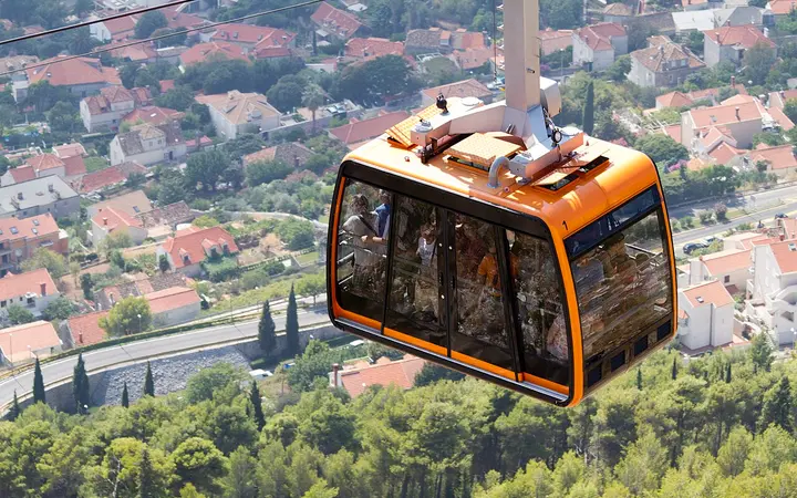 Orange Dubrovnik cable car cabin above the city's houses and pine trees