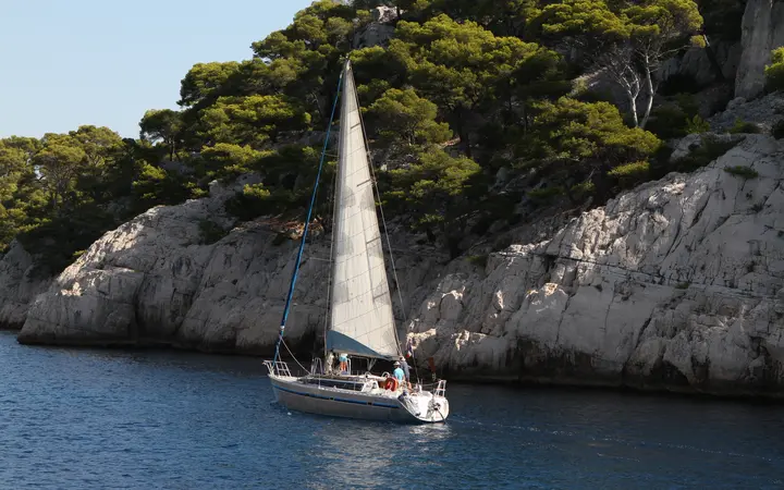 A sailing boat moored below pine-topped limestone cliffs in the Calanques near Marseille