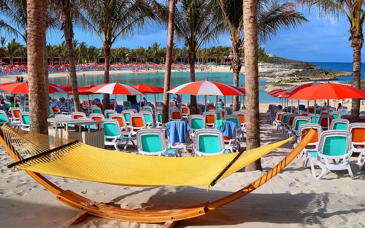 Hammock, loungers and red umbrellas under palm trees at Hideaway Beach, CocoCay