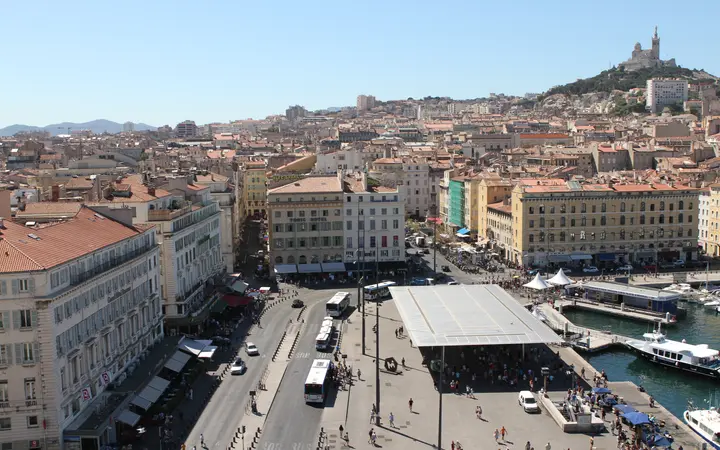 The Quai des Belges and the Ombrière canopy at Marseille's Vieux-Port, with Notre-Dame de la Garde on the hill behind