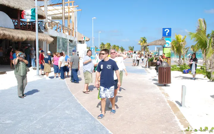 Visitors walking along the paved beachfront Malecón promenade in Mahahual, lined with palapa-roofed bars and palm trees