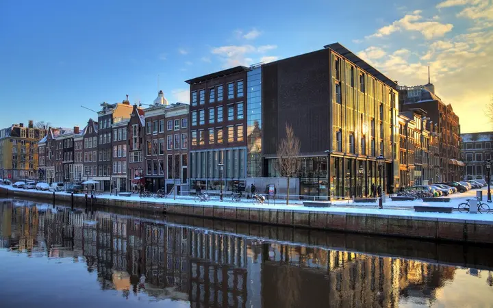 The Anne Frank House and neighbouring canal houses along the Prinsengracht, reflected in the still canal water in bright daylight
