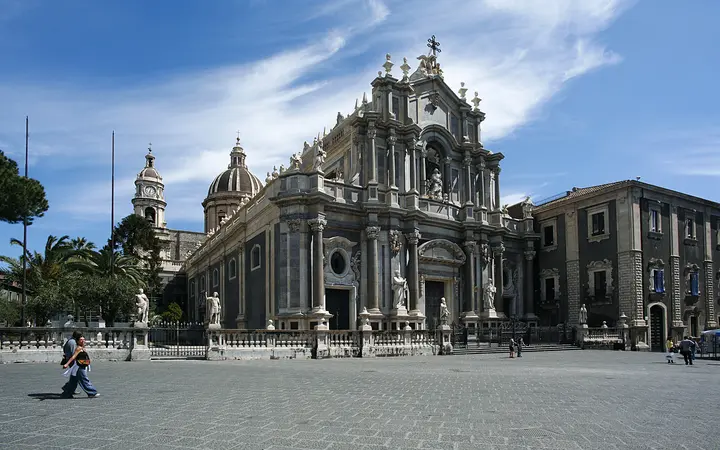 The Baroque façade and dome of Catania Cathedral of Sant'Agata on Piazza del Duomo under a blue sky with light clouds