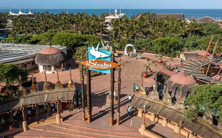 Elevated daylight view of the uShaka Marine World entrance arch and Village Walk with palms, the Phantom Ship and the sea behind