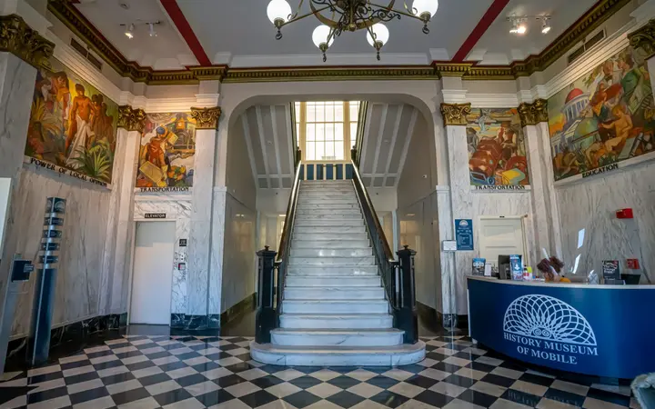 Interior entrance hall of the History Museum of Mobile with a marble staircase, chequered floor and murals