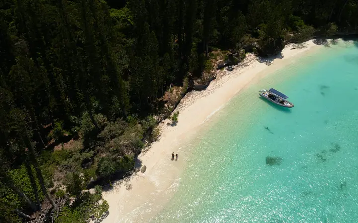 Aerial view of a white beach, a moored boat and turquoise shallows at Îlot Brosse.
