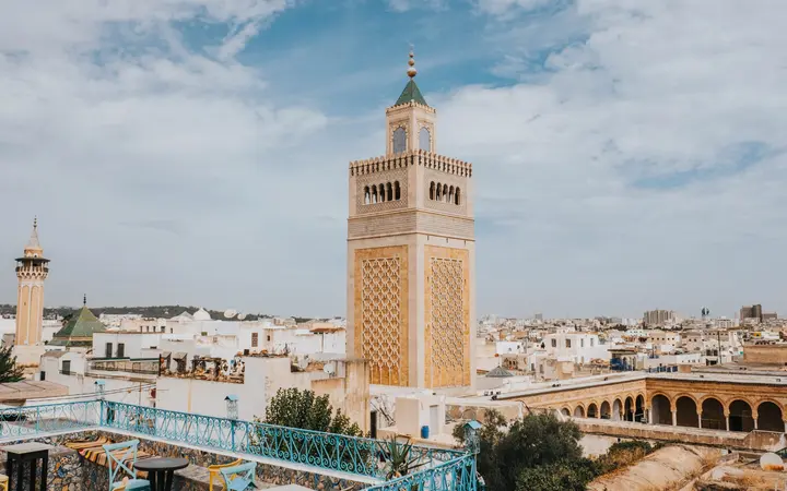The square minaret of the Zitouna Mosque rising above the rooftops of the Tunis medina in daylight, seen from a terrace