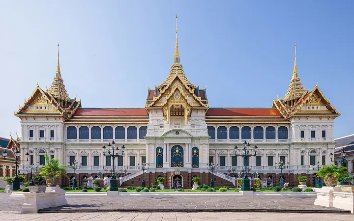 The white-and-gold Chakri Maha Prasat throne hall at the Grand Palace, Bangkok, under a clear blue sky.