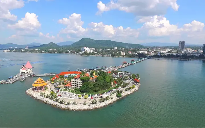 Ko Loi island in Si Racha with its Chinese temple, linked to the shore by a causeway, under a blue sky.