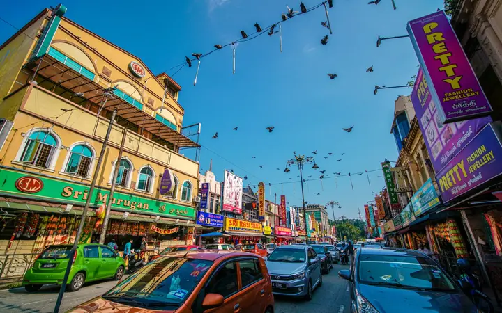 Colourful shopfronts, banners and parked cars along Jalan Tengku Kelana in Little India, Klang, under a blue sky