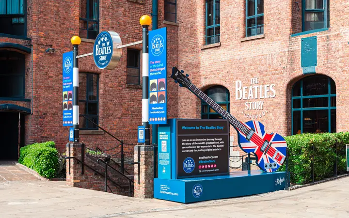 The red-brick entrance of The Beatles Story at the Royal Albert Dock with blue signage and a large Union Jack guitar sculpture