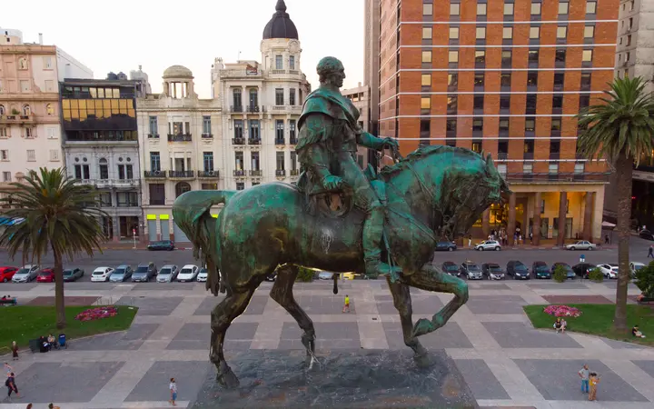 Equestrian statue of José Artigas in Plaza Independencia, Montevideo, with palm trees and historic buildings under a blue sky