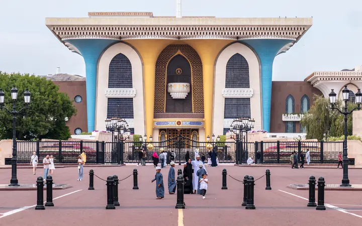 Al Alam Palace's blue and gold columned facade across a wide plaza in Old Muscat.