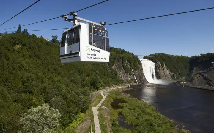 Cable car above the green gorge at Montmorency Falls on a sunny summer day, with the waterfall in the background.