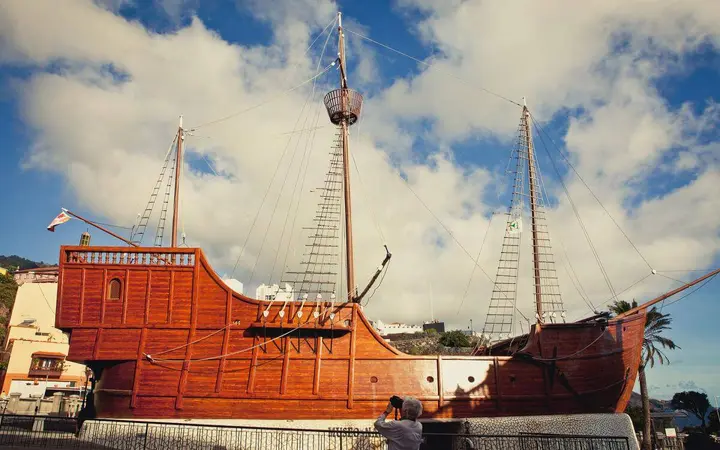 The Barco de la Virgen ship replica with its masts and red hull under a blue sky in Santa Cruz de La Palma.