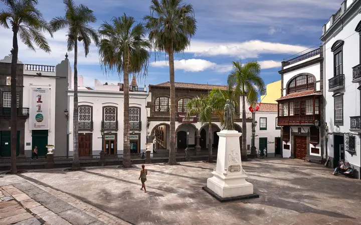 Plaza de España in Santa Cruz de La Palma with palm trees and whitewashed colonial buildings under a blue sky.