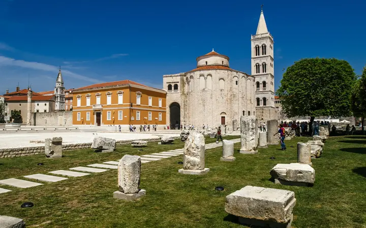 Stone column fragments on the grass of the Roman Forum in Zadar with St Donatus Church and the bell tower behind